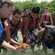 A young woman standing in knee high water holds a sea star as a group of teens gathers to see it